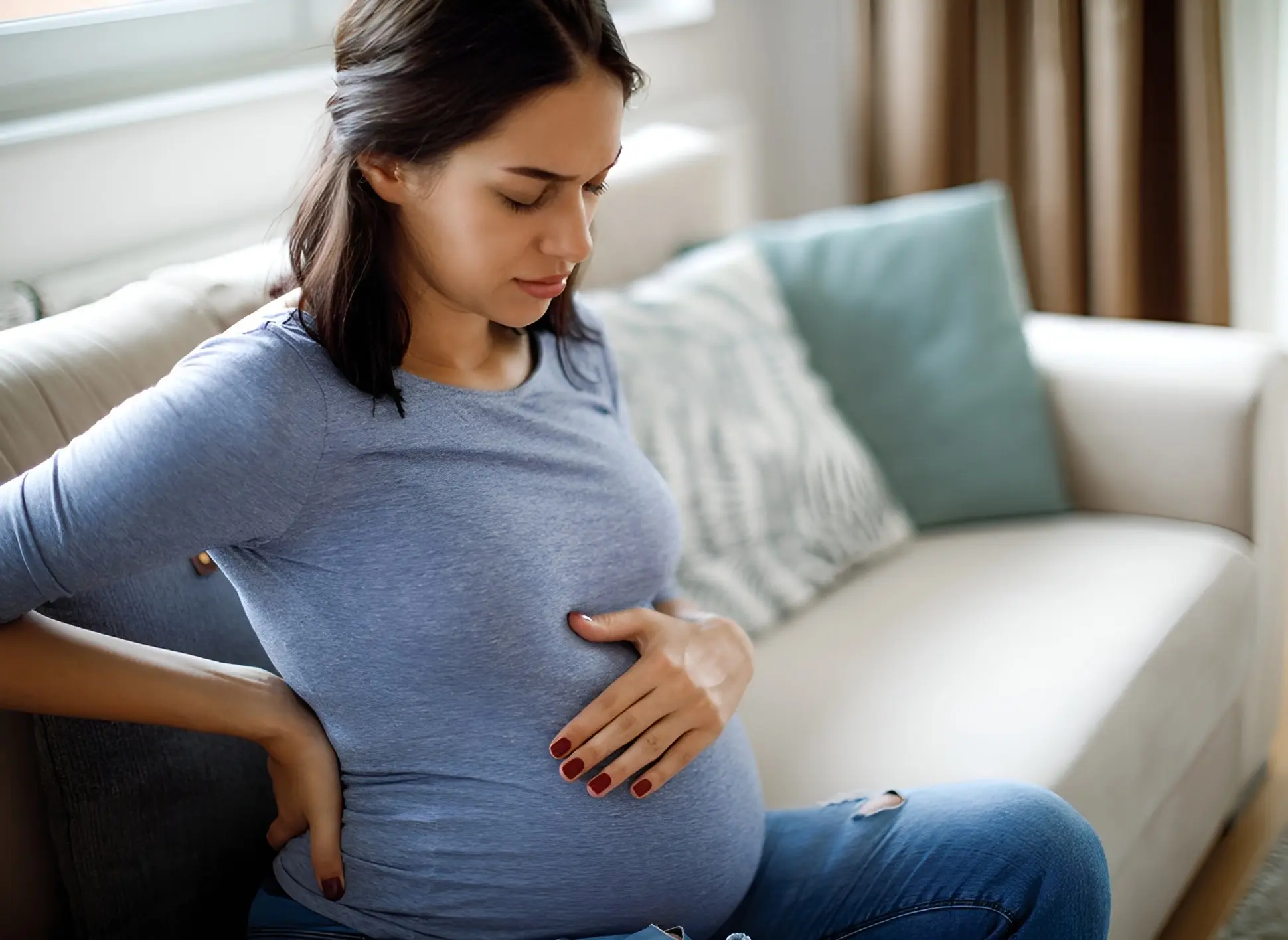 Pregnant woman sitting on a sofa, experiencing common physical discomforts during pregnancy.