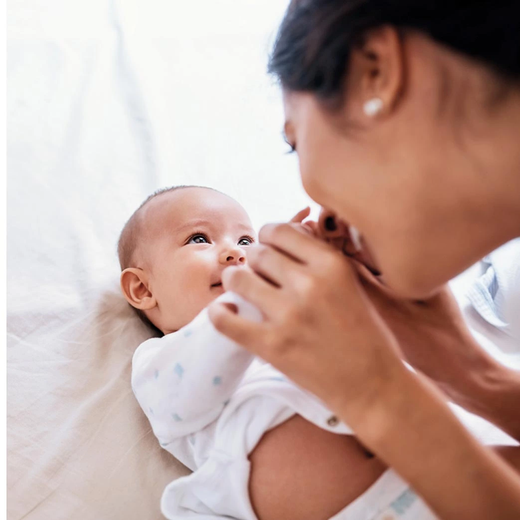 Mother kissing newborn baby's hands on white blanket
