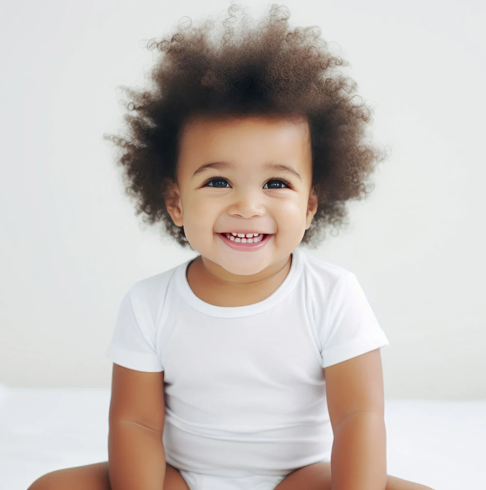 Smiling toddler wearing white shirt, sitting happily.