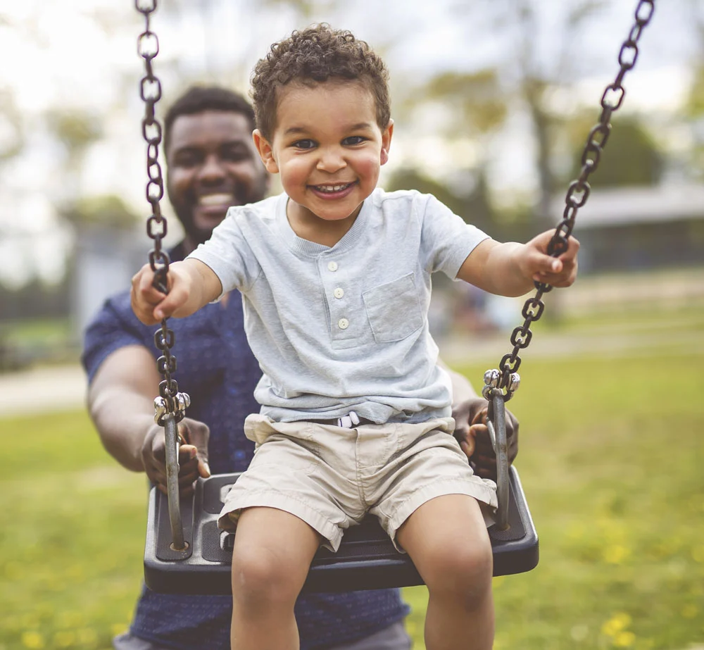 Father pushing toddler on swing