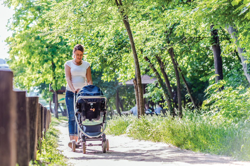 Woman happily pushing stroller on a sunny path.