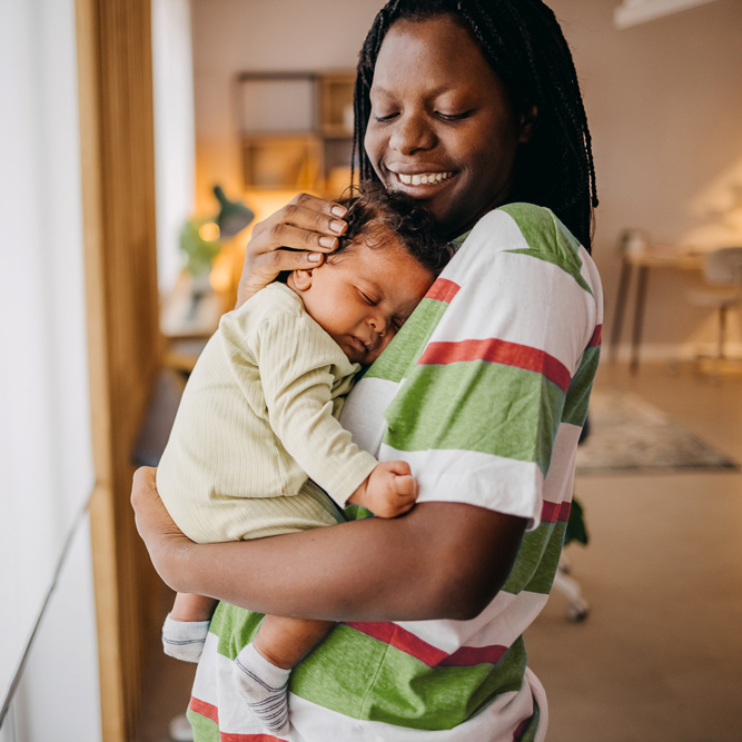 Smiling woman cradling a sleeping baby warmly.