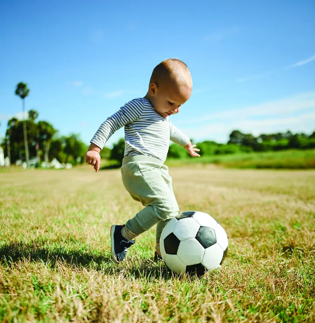 Toddler kicking soccer ball on grassy field
