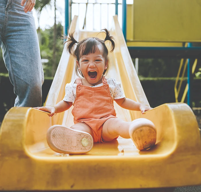 Girl joyfully sliding down a playground slide